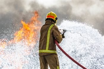 Uniformed firefighter attempting to extinguish a fire.