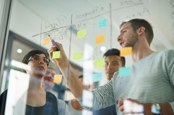 Colleagues looking at a plan written on glass in whiteboard pen. They also have some sticky notes.