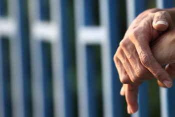 Close up of the hands of an offender leaning through prison railings.