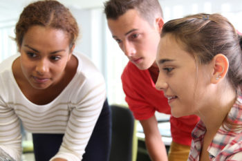 Three students looking at a screen together in a college environment.