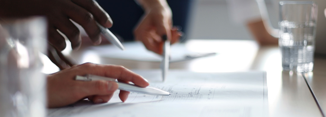 Close up of three people holding pens to a piece of paper on a desk.