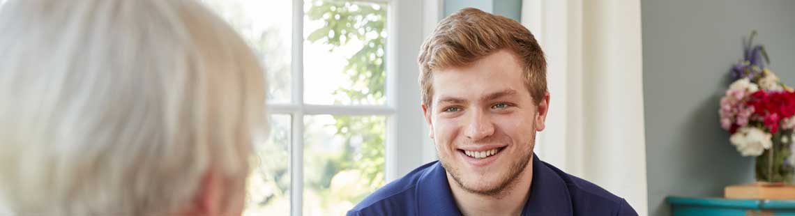 Social worker making notes on a clipboard while chatting to a patient in their home.