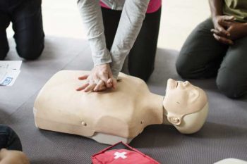 People circling a first aid dummy, taking part in a first aid course.