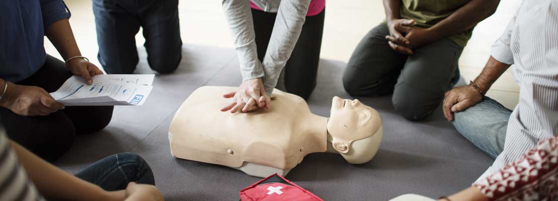 People circling a first aid dummy, taking part in a first aid course.