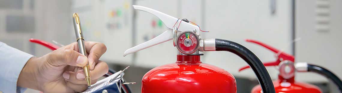 Someone inspecting fire extinguishers, they use a pen to make notes on paper on a clipboard