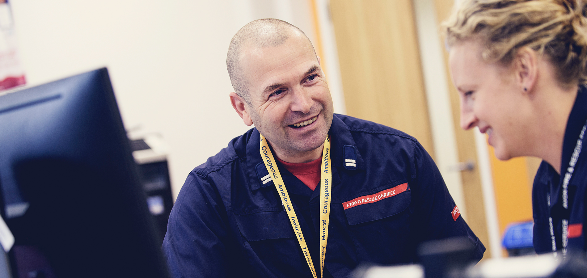 Two fire and rescue service staff talking together in an office environment.