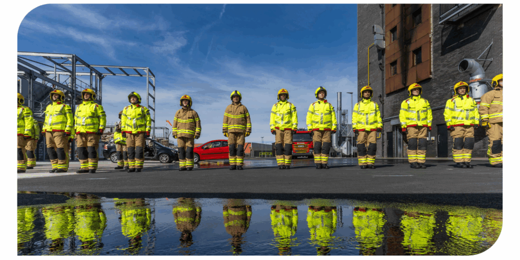 Firefighters in uniform lined up in the grounds of a fire station.